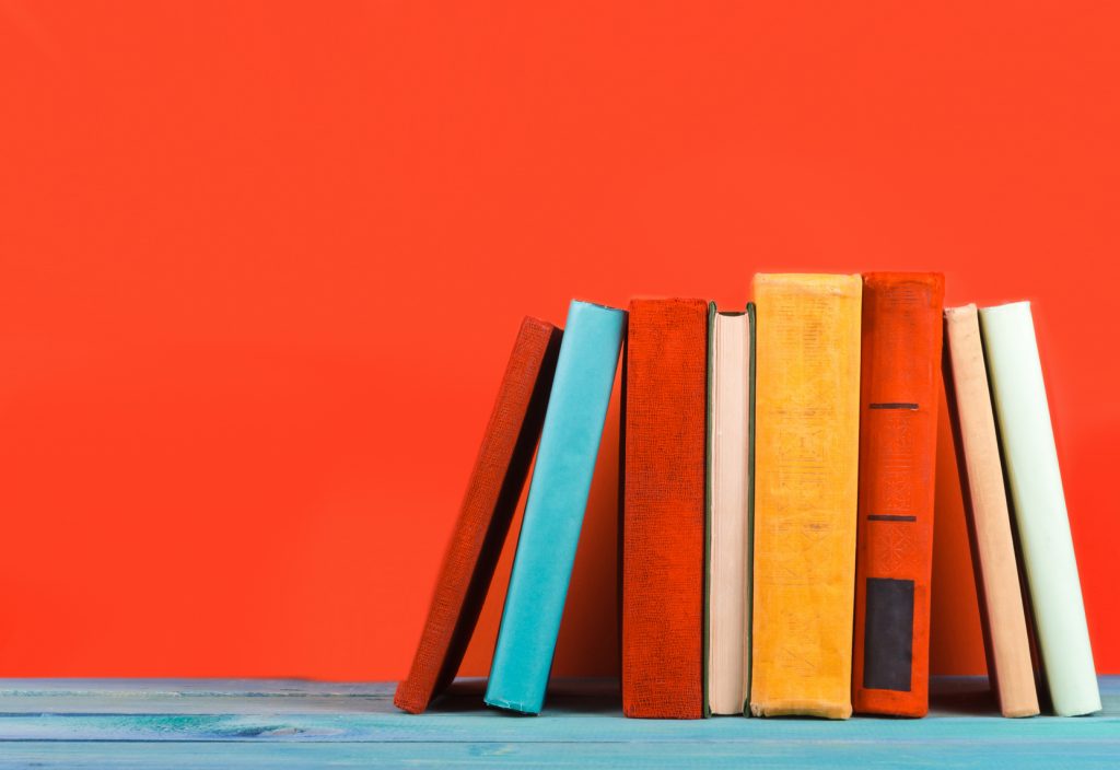 Composition with vintage old hardback books, diary, fanned pages on wooden deck table and red background. Books stacking. Back to school. Copy Space. Education background.